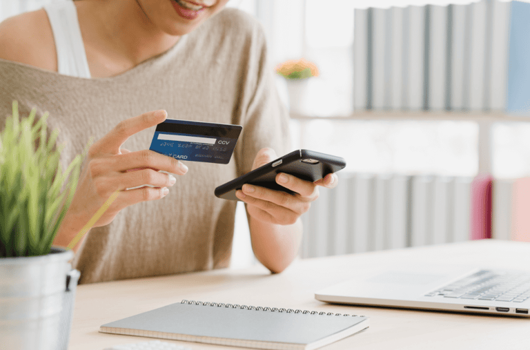 Mulher com cartão de crédito realizando pagamento online pelo celular.