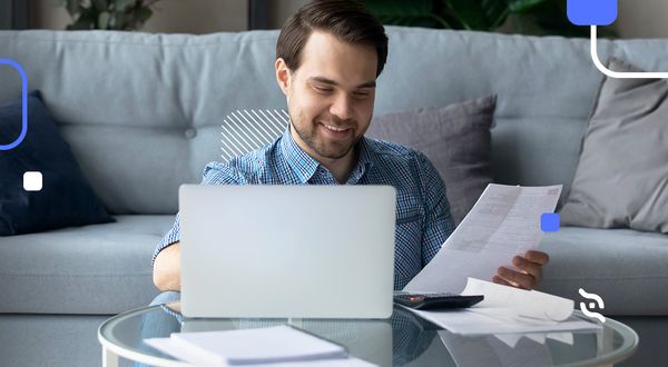 homem com barba sentado em sofá, segurando boletos, fazendo parcelamento sem cartão de crédito pelo notebook