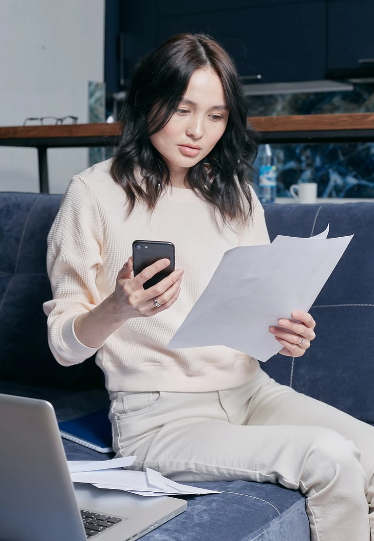 mulher asiática sentada em sofá, segurando smartphone e boletos, fazendo parcelamento sem cartão de crédito